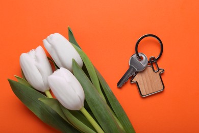 Photo of Beautiful spring flowers and key with trinket in shape of house on orange background, flat lay