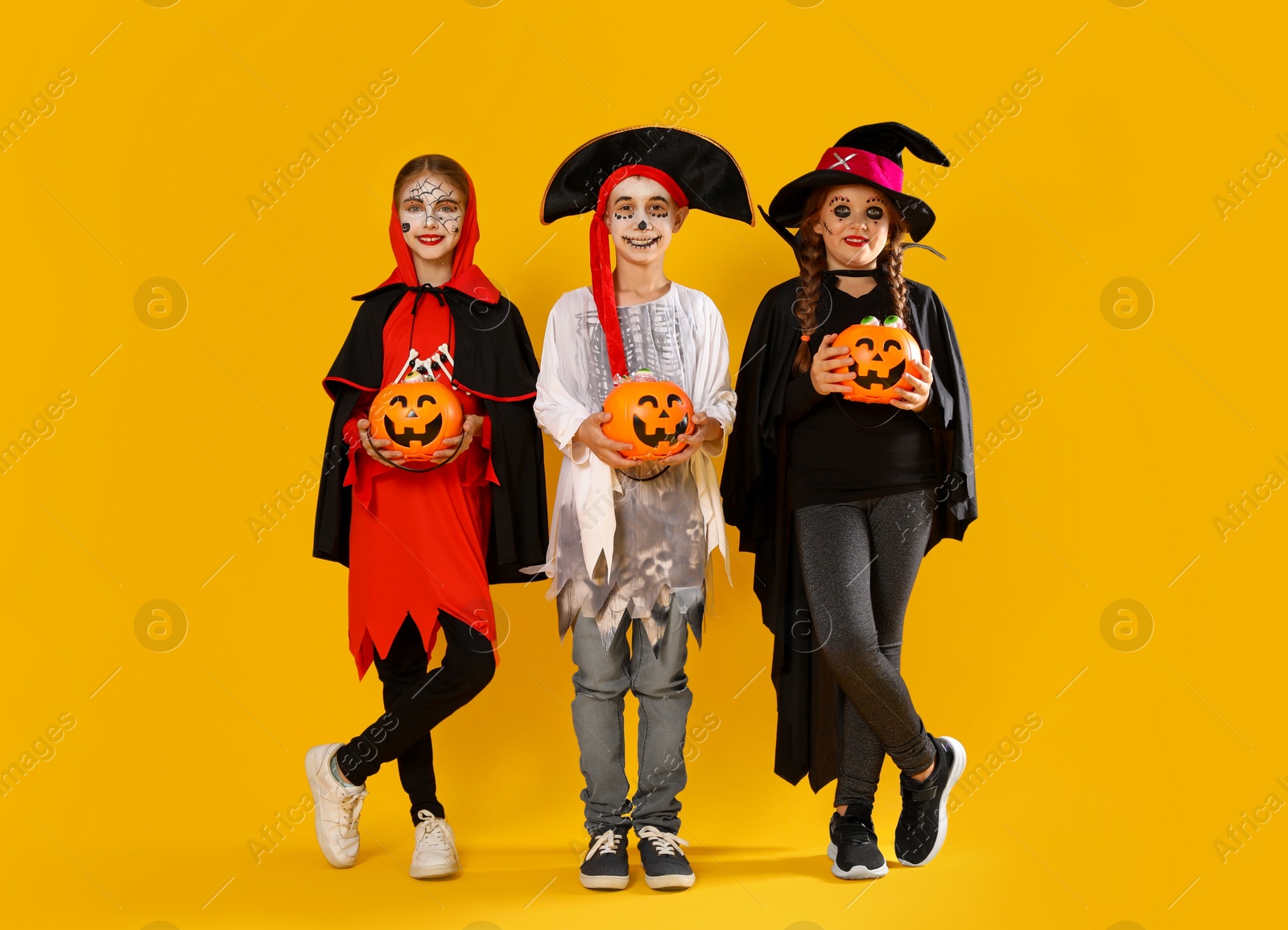 Photo of Cute little kids with pumpkin candy buckets wearing Halloween costumes on yellow background