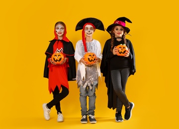 Photo of Cute little kids with pumpkin candy buckets wearing Halloween costumes on yellow background