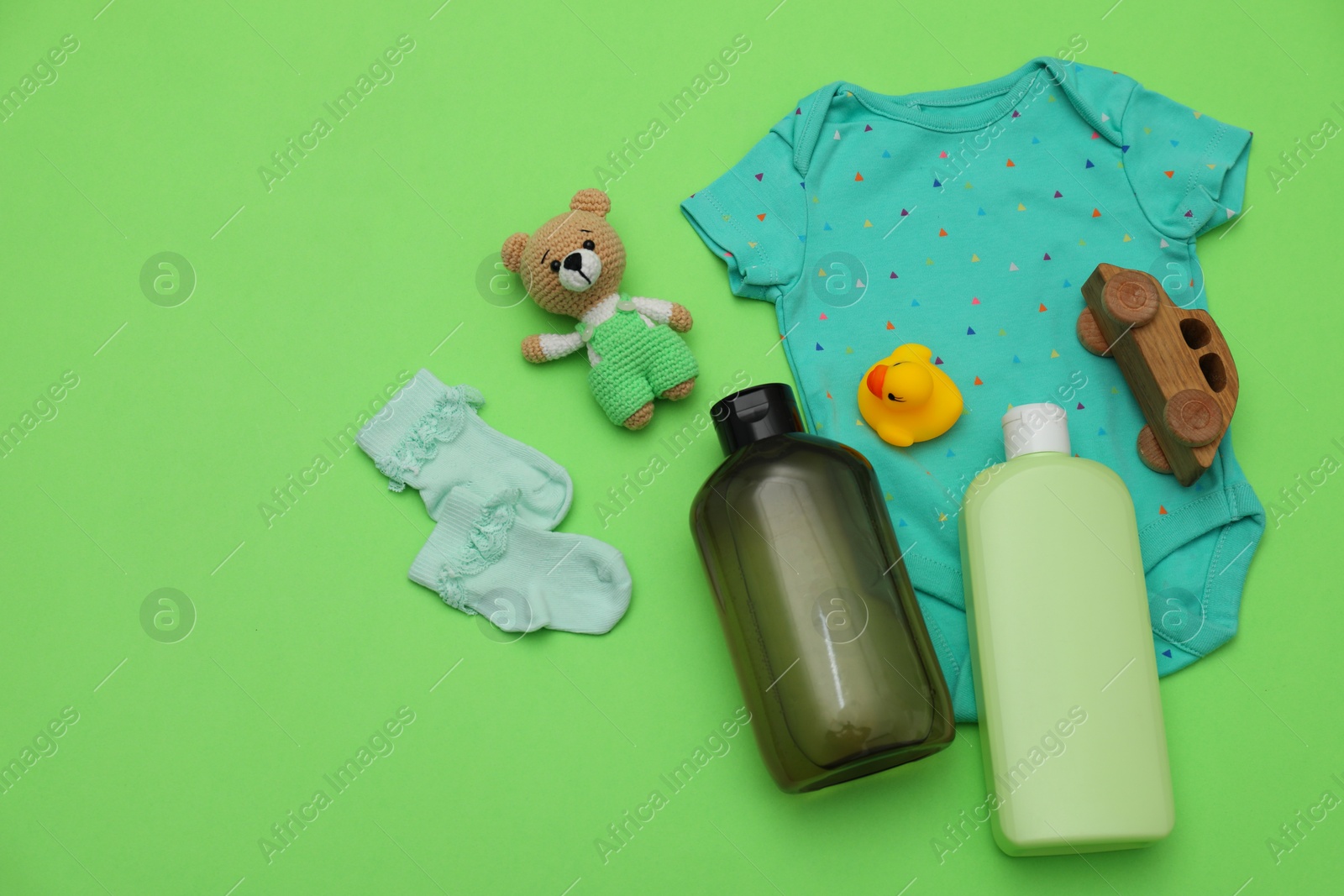 Photo of Bottles of laundry detergents, baby clothes and toys on light green background, flat lay. Space for text