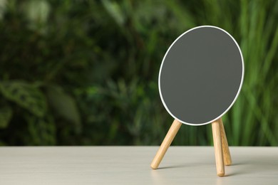 Photo of Stylish round mirror on white table against blurred background. Space for text