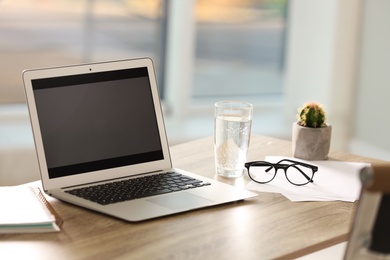 Modern laptop and glass of water on table in office