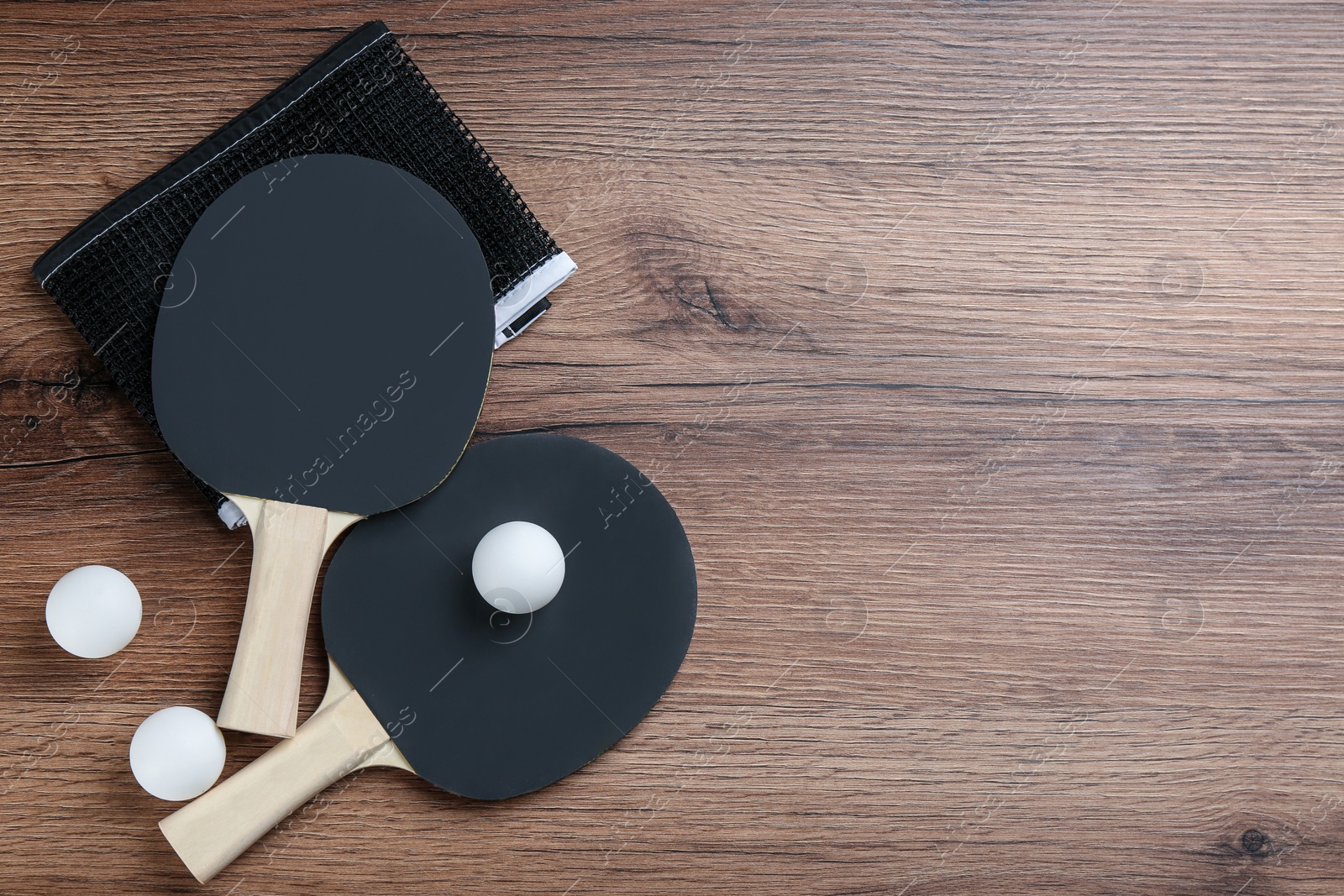 Photo of Ping pong rackets, net and balls on wooden table, flat lay. Space for text