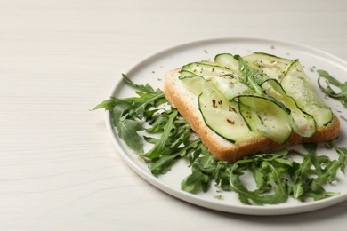 Tasty cucumber sandwich with seasoning and arugula on white wooden table, space for text