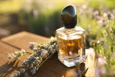 Bottle of luxury perfume and lavender flowers on wooden table in blooming field. Space for text