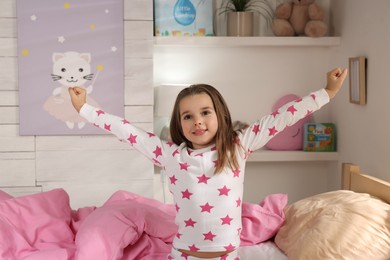 Photo of Cute little girl stretching near bed at home
