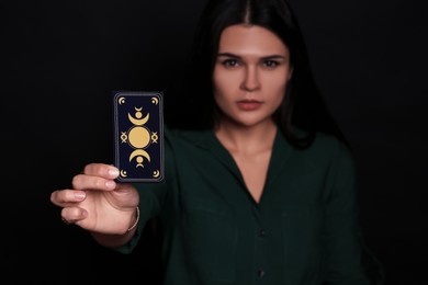 Soothsayer predicting future against black background, closeup. Focus on tarot card