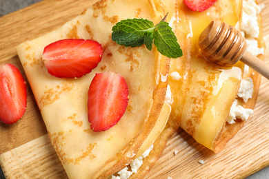 Delicious thin pancakes with strawberries, cottage cheese and honey on wooden board, closeup