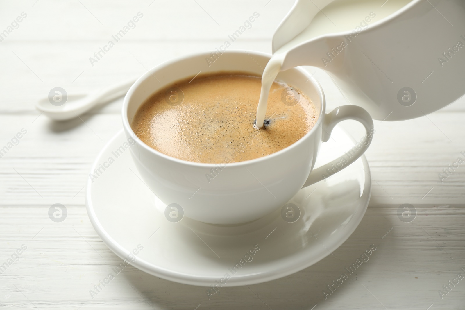 Photo of Pouring milk into cup of hot coffee on white wooden table