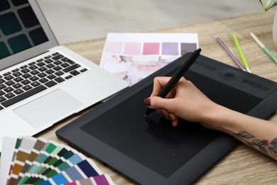 Professional designer with graphic tablet at wooden table, closeup