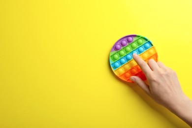 Photo of Woman using pop it fidget toy on yellow background, top view. Space for text
