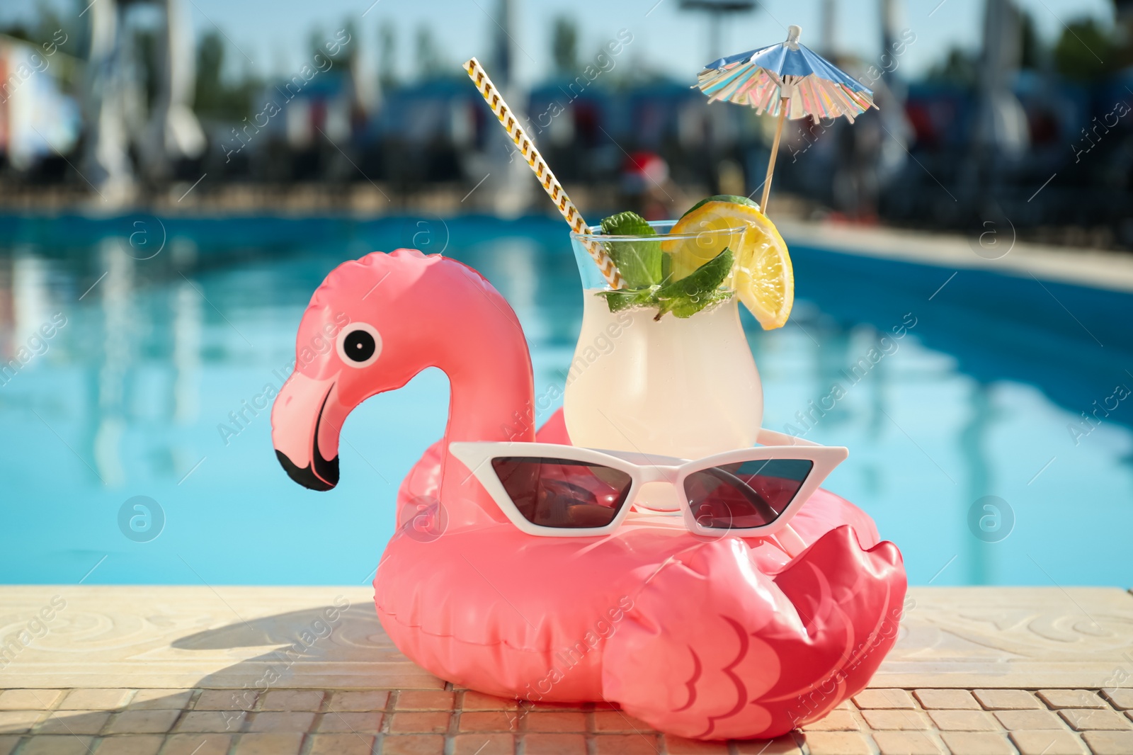 Photo of Tasty refreshing cocktail and sunglasses on edge of swimming pool. Party items