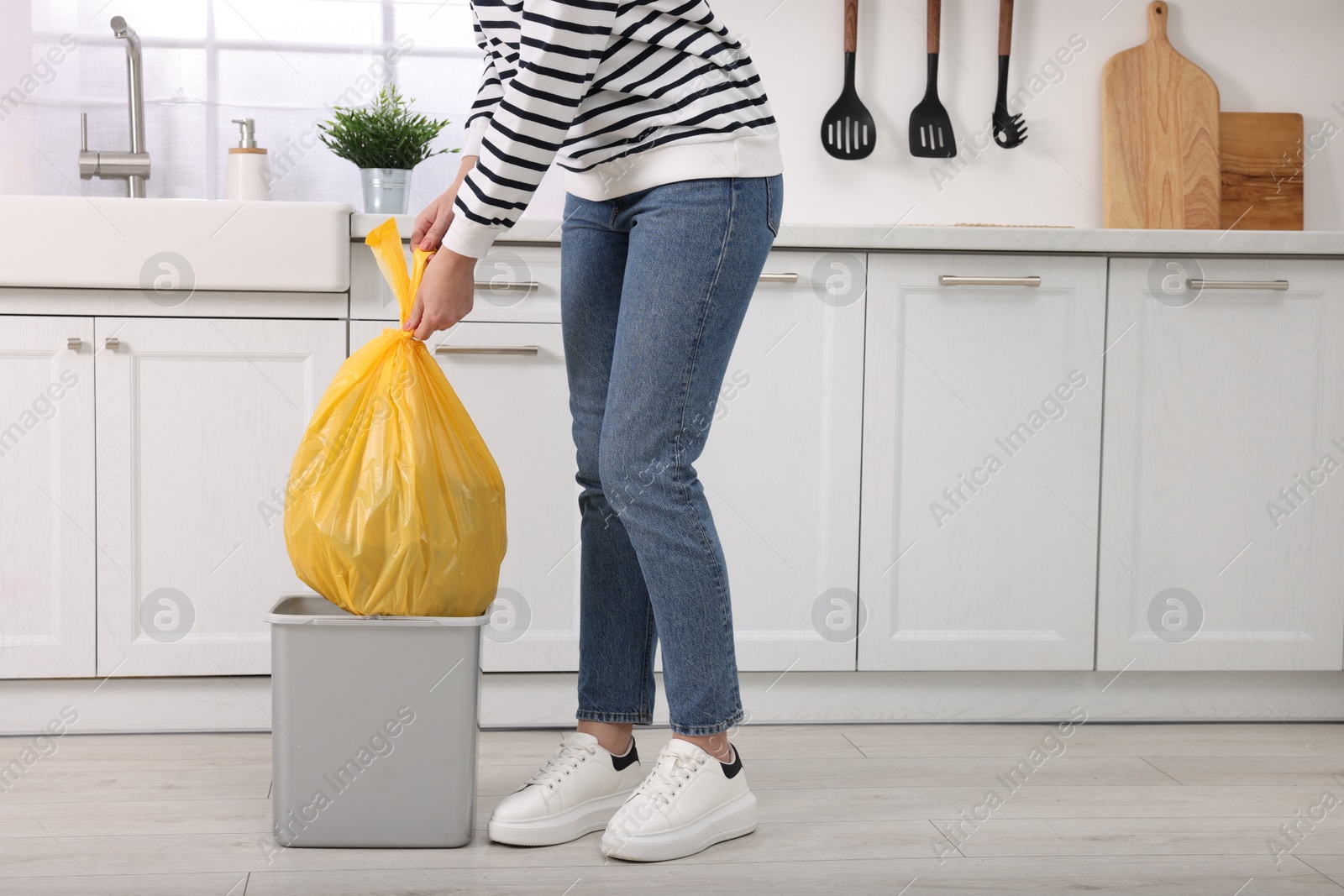 Photo of Woman taking garbage bag out of trash bin in kitchen, closeup