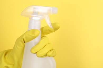 Photo of Woman holding plastic spray bottle on yellow background, closeup. Space for text