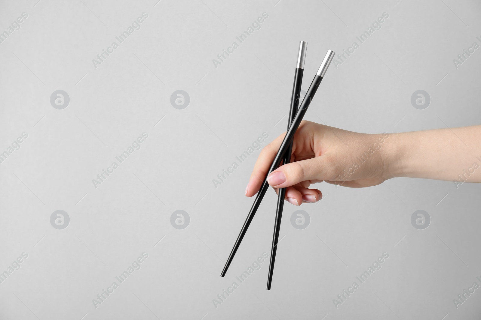 Photo of Woman holding pair of black chopsticks on light grey background, closeup. Space for text