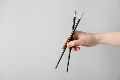 Photo of Woman holding pair of black chopsticks on light grey background, closeup. Space for text