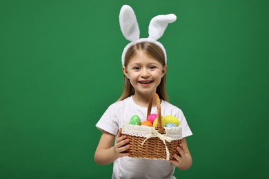 Easter celebration. Cute girl with bunny ears holding basket of painted eggs on green background