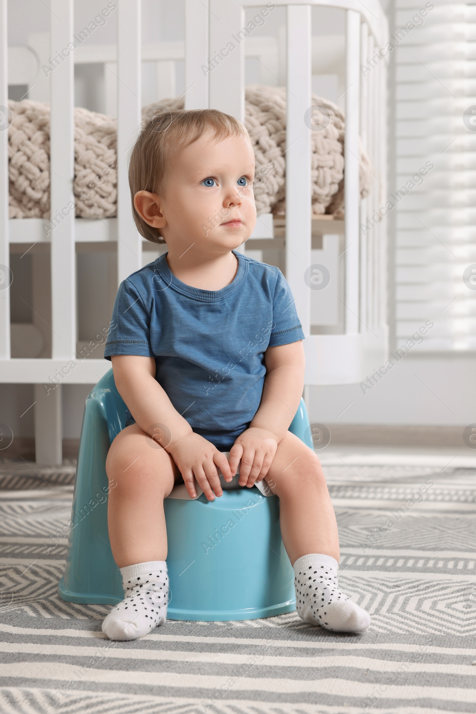 Photo of Little child sitting on plastic baby potty indoors