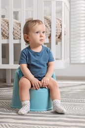 Little child sitting on plastic baby potty indoors