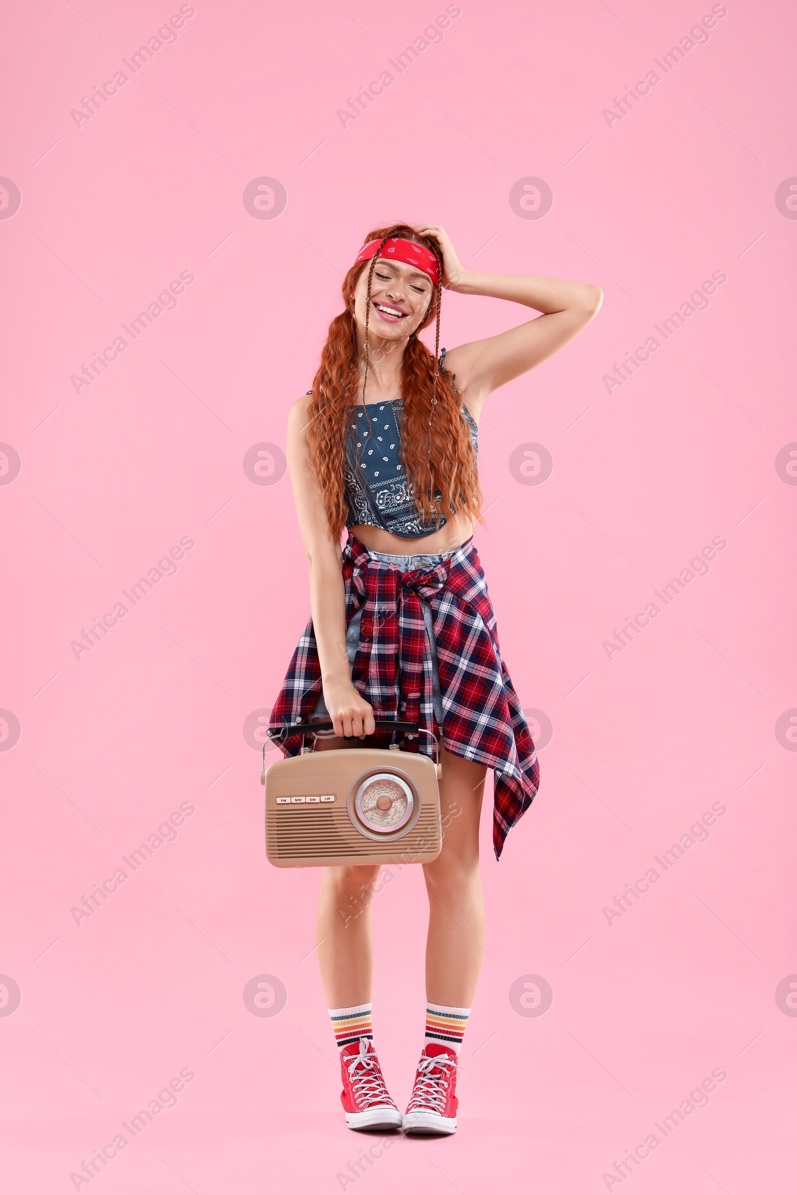 Photo of Stylish young hippie woman with retro radio receiver on pink background