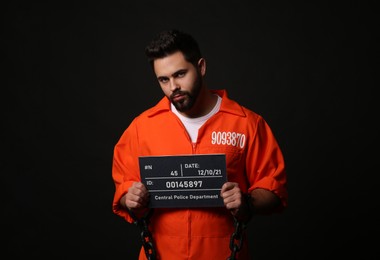Photo of Prisoner with chained hands holding mugshot letter board on black background