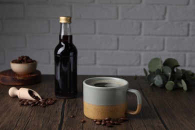 Bottle with delicious syrup, mug of aromatic coffee and beans on wooden table