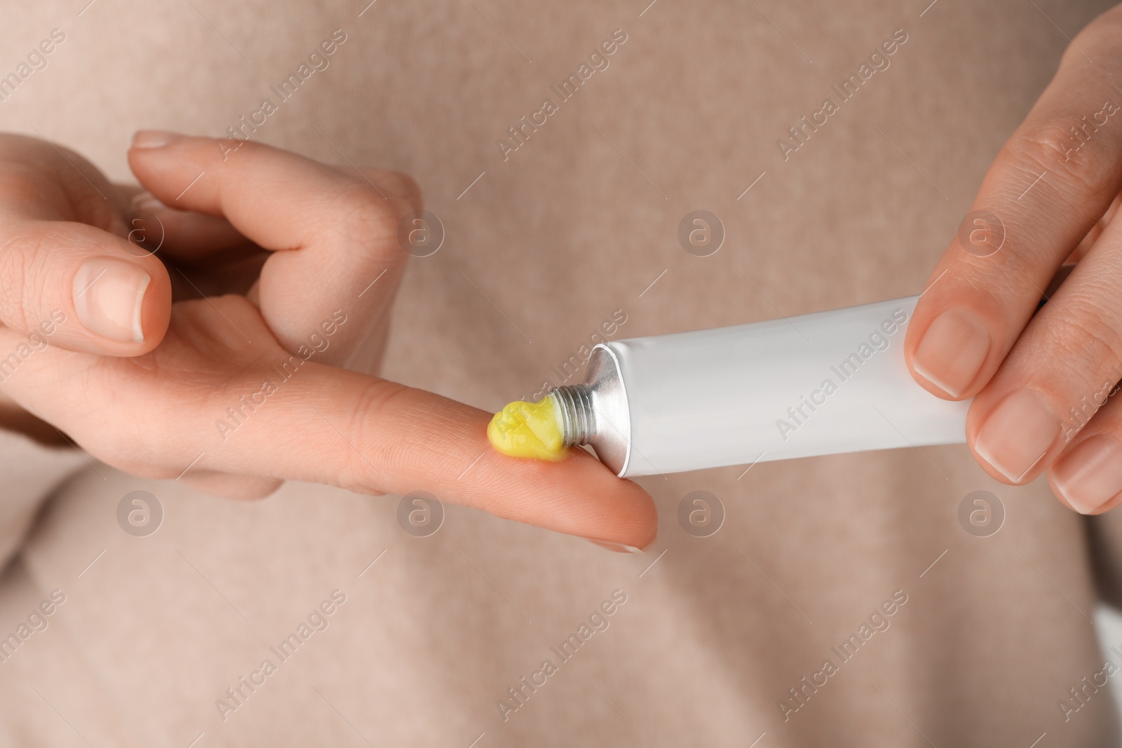 Photo of Woman squeezing out ointment from tube on her finger, closeup