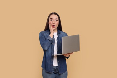 Photo of Surprised young woman with laptop on beige background