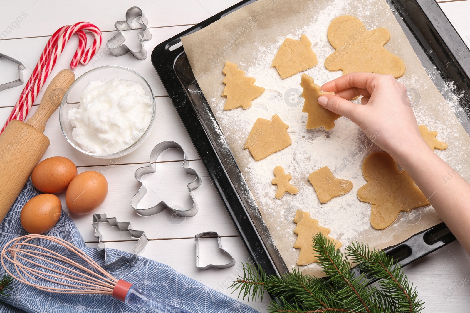 Photo of Woman putting raw Christmas cookies on baking tray at white wooden table, top view