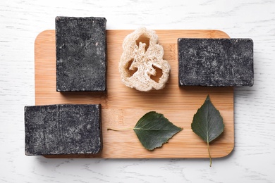 Photo of Natural tar soap and loofah on white wooden table, top view