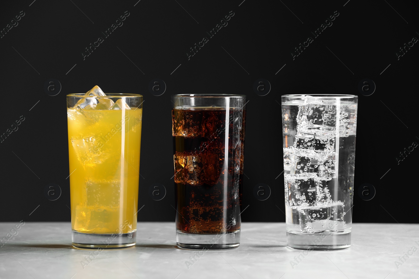 Photo of Glasses of different refreshing soda water with ice cubes on white marble table