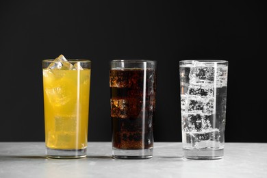 Glasses of different refreshing soda water with ice cubes on white marble table