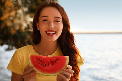 Photo of Beautiful young woman with watermelon near river at sunset