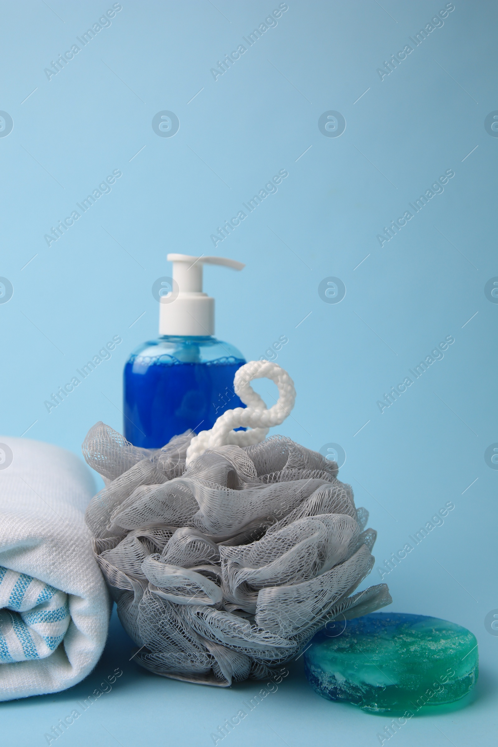 Photo of Grey shower puff, cosmetic products and towel on light blue background, space for text