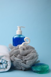 Grey shower puff, cosmetic products and towel on light blue background, space for text