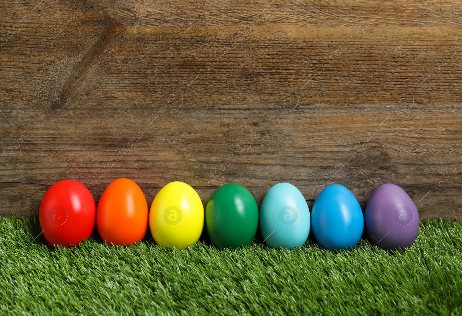 Photo of Bright Easter eggs on green grass against wooden background