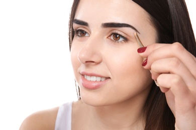 Photo of Young woman plucking eyebrows with tweezers, indoors