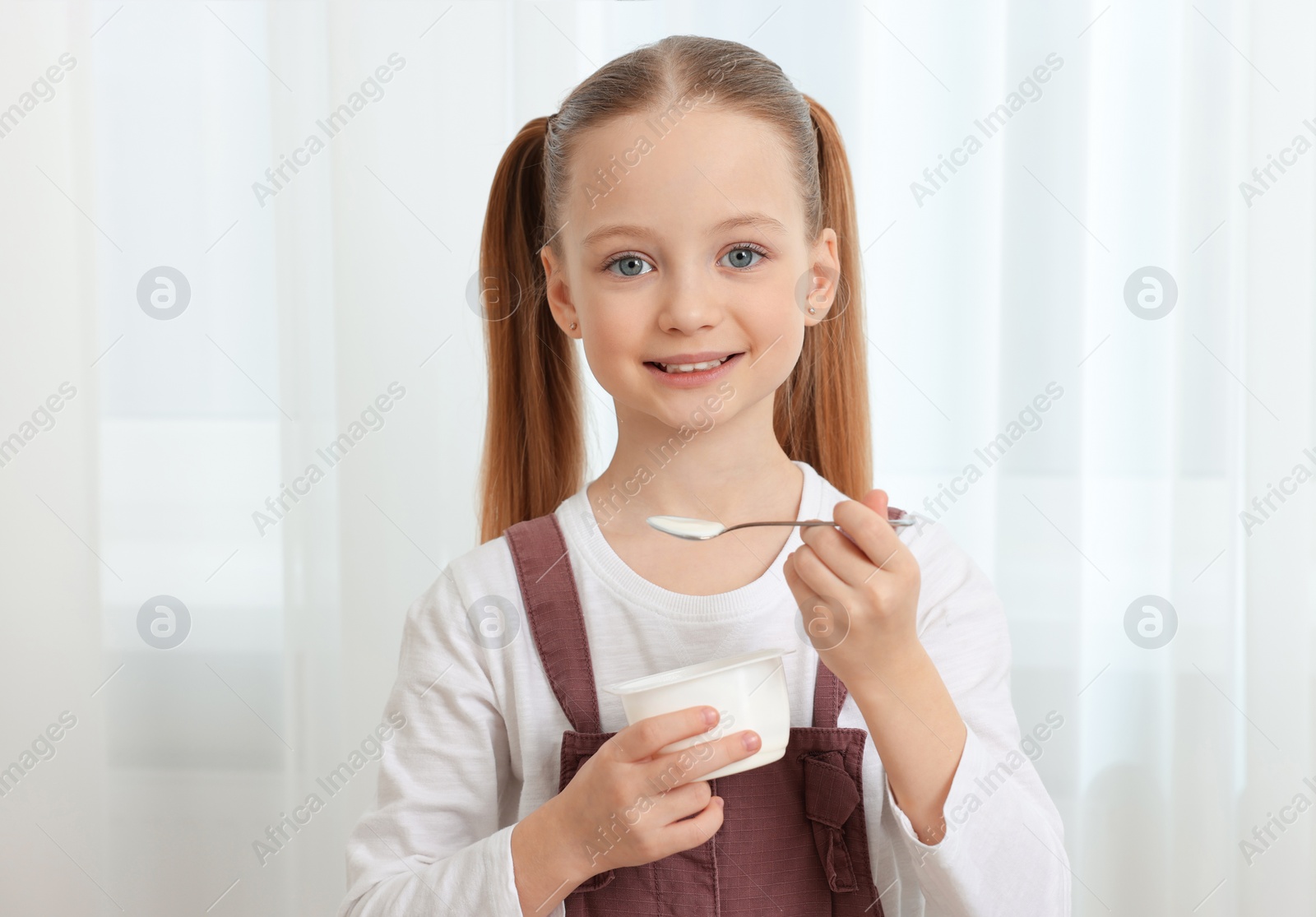 Photo of Cute little girl with tasty yogurt indoors
