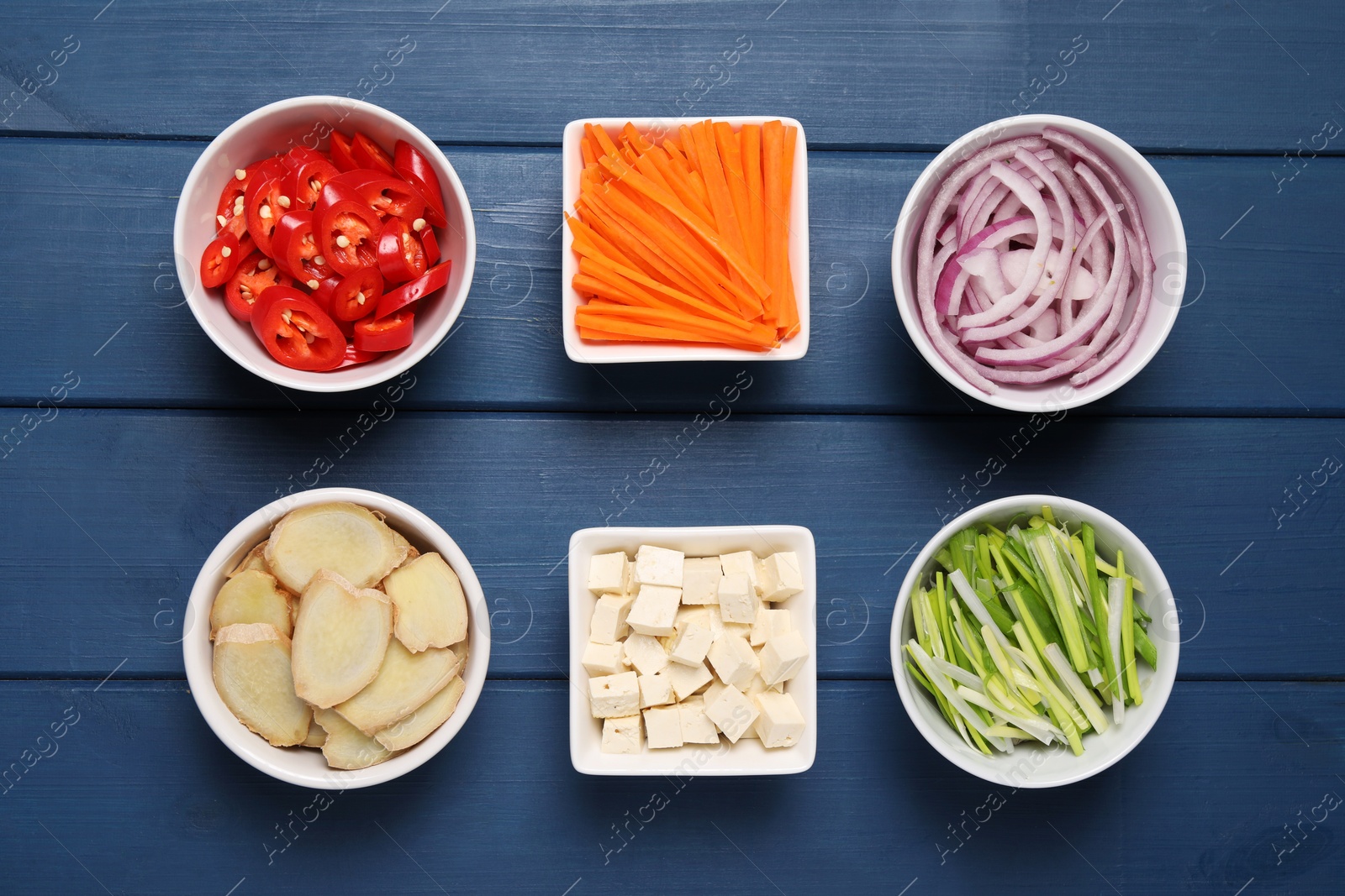 Photo of Cooking delicious ramen soup. Different fresh ingredients in bowls on blue wooden table, flat lay