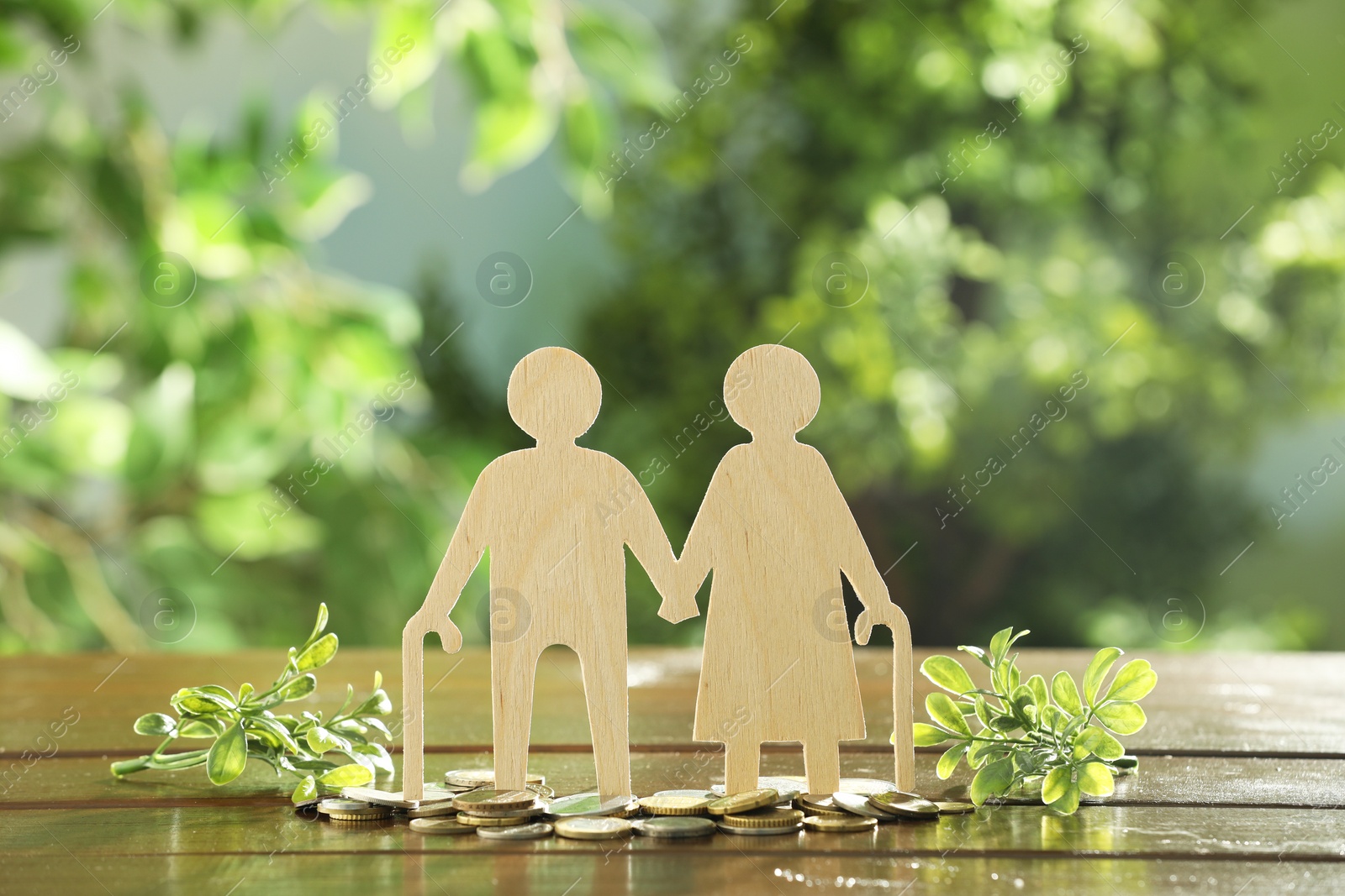 Photo of Pension savings. Figure of senior couple, coins and green twigs on wooden table outdoors