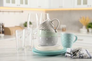 Many different clean dishware, cutlery, glasses and cups on white marble table in kitchen