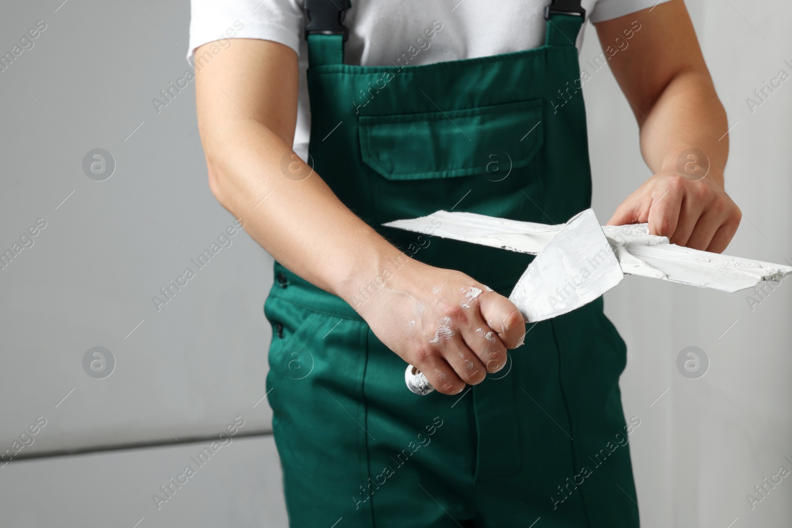 Photo of Professional worker holding putty knives with plaster indoors, closeup. Space for text