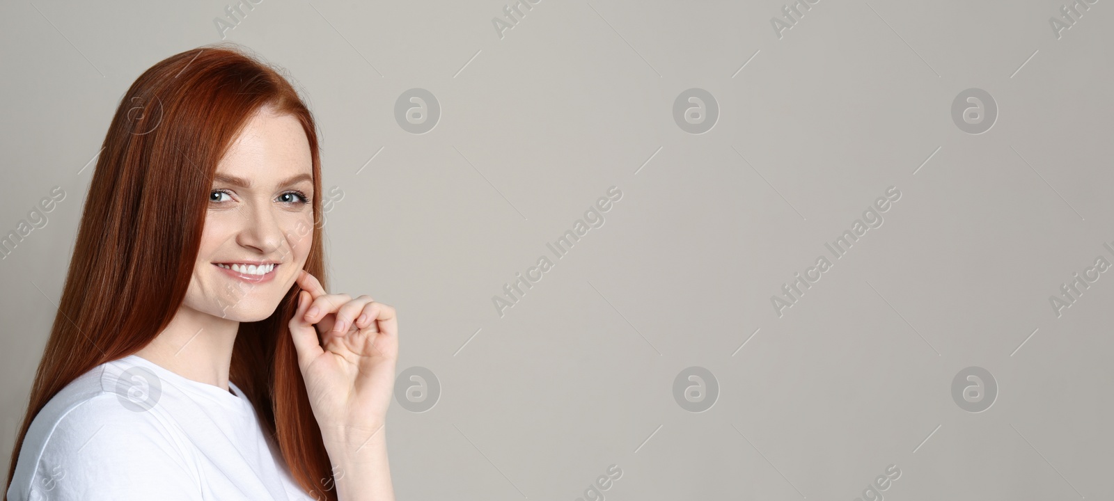 Photo of Candid portrait of happy young woman with charming smile and gorgeous red hair on beige background, space for text