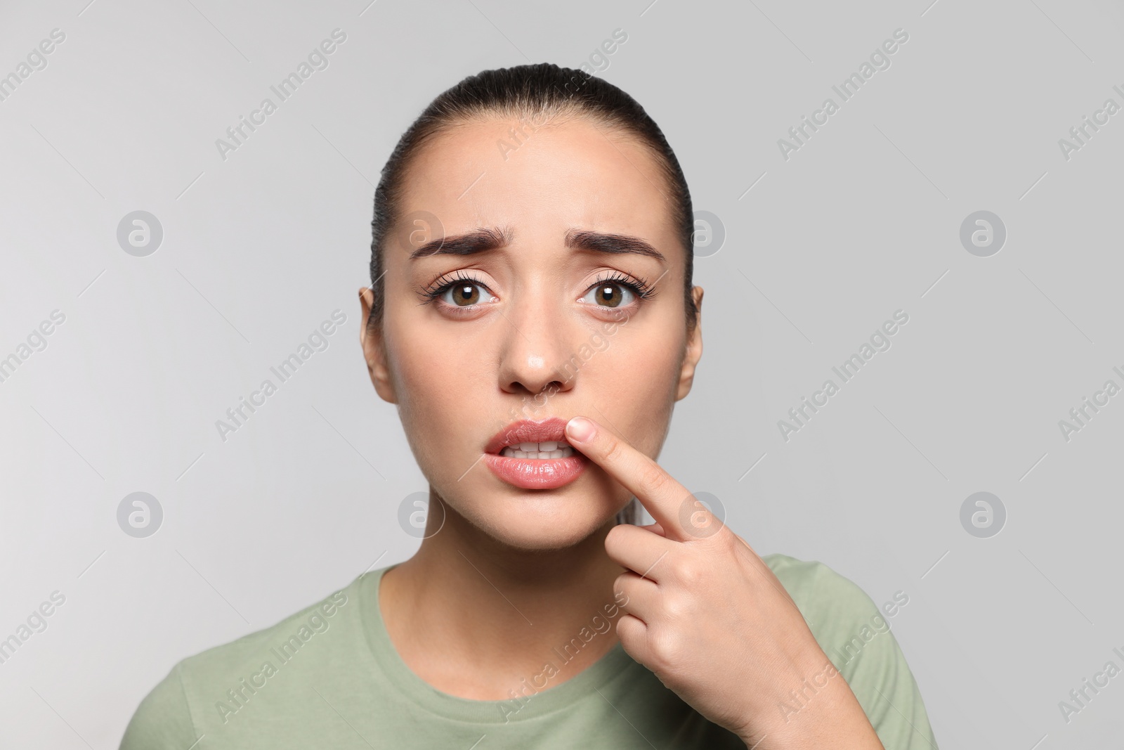 Photo of Emotional woman with herpes touching lips on light grey background