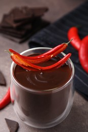 Photo of Delicious hot chocolate with chili peppers on brown textured table, closeup