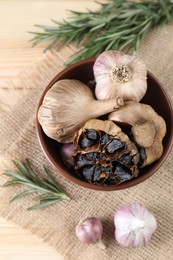 Bulbs of fresh and fermented black garlic on wooden table, flat lay