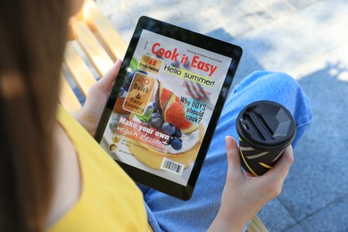 Photo of Woman with coffee reading online magazine on tablet outdoors, closeup