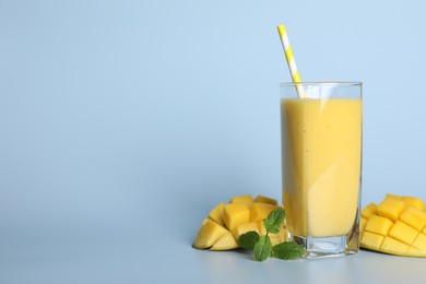 Photo of Glass of tasty smoothie with straw, mango and mint leaves on light blue background. Space for text