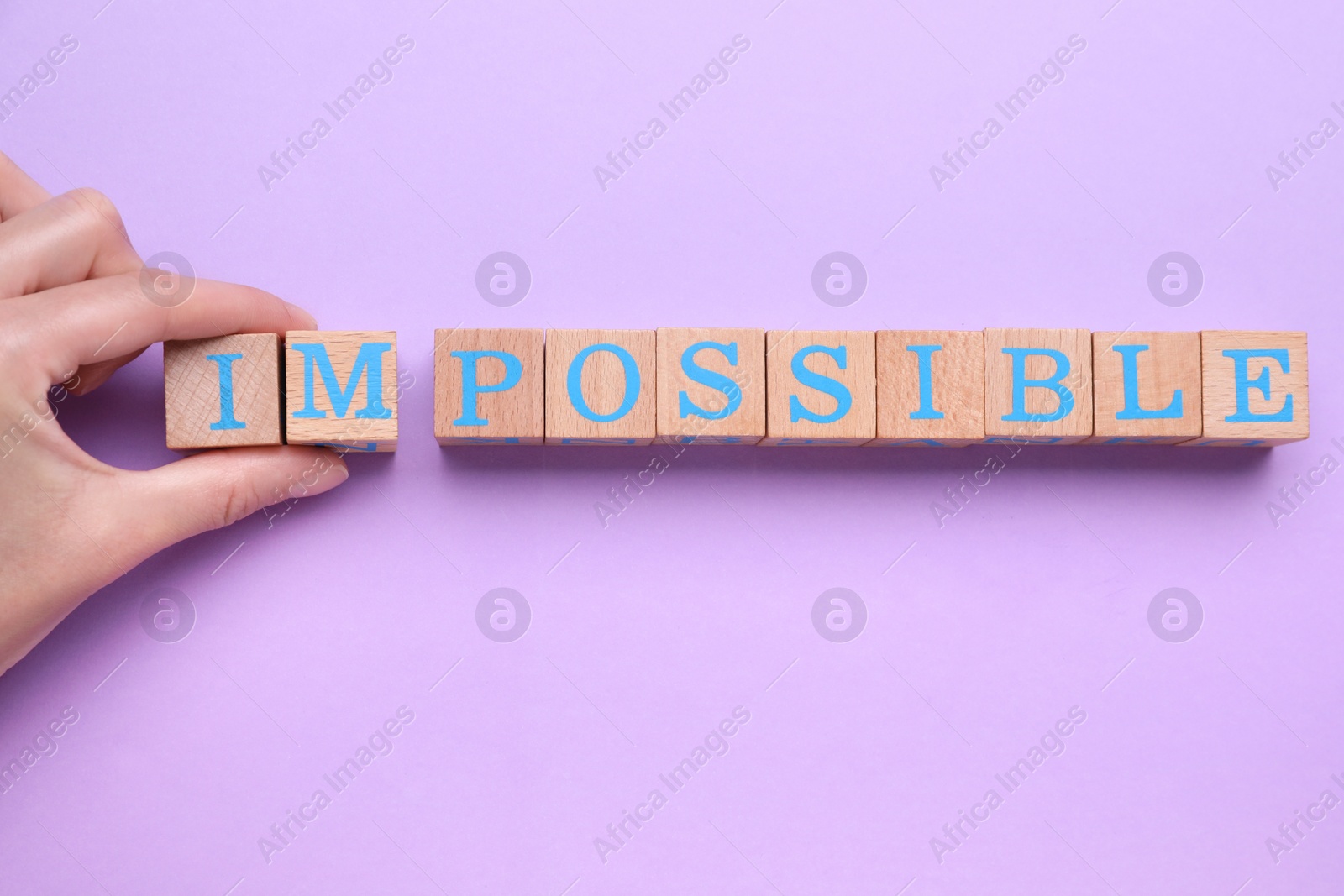 Photo of Motivation concept. Woman changing word from Impossible into Possible by removing wooden cubes on violet background, top view
