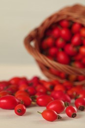 Photo of Ripe rose hip berries with wicker basket on white wooden table, closeup. Space for text